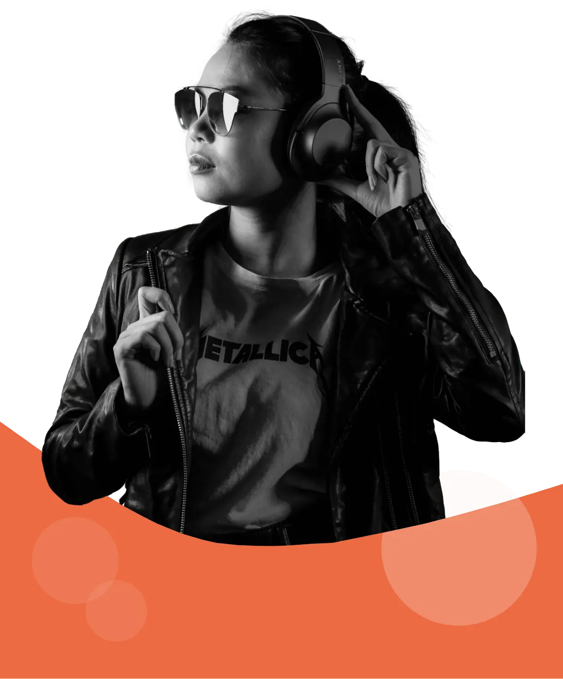 In black and white, a black haired woman in a leather jacket, sunglasses and wearing large headphones, facing her left. She's holding one of the ears of her headphones with one hand and the lapel of her jacket with the other. Her shirt has the logo of metal band "Metallica". Her lower body is partially obstructed by a curved shape in Magroove's orange color.